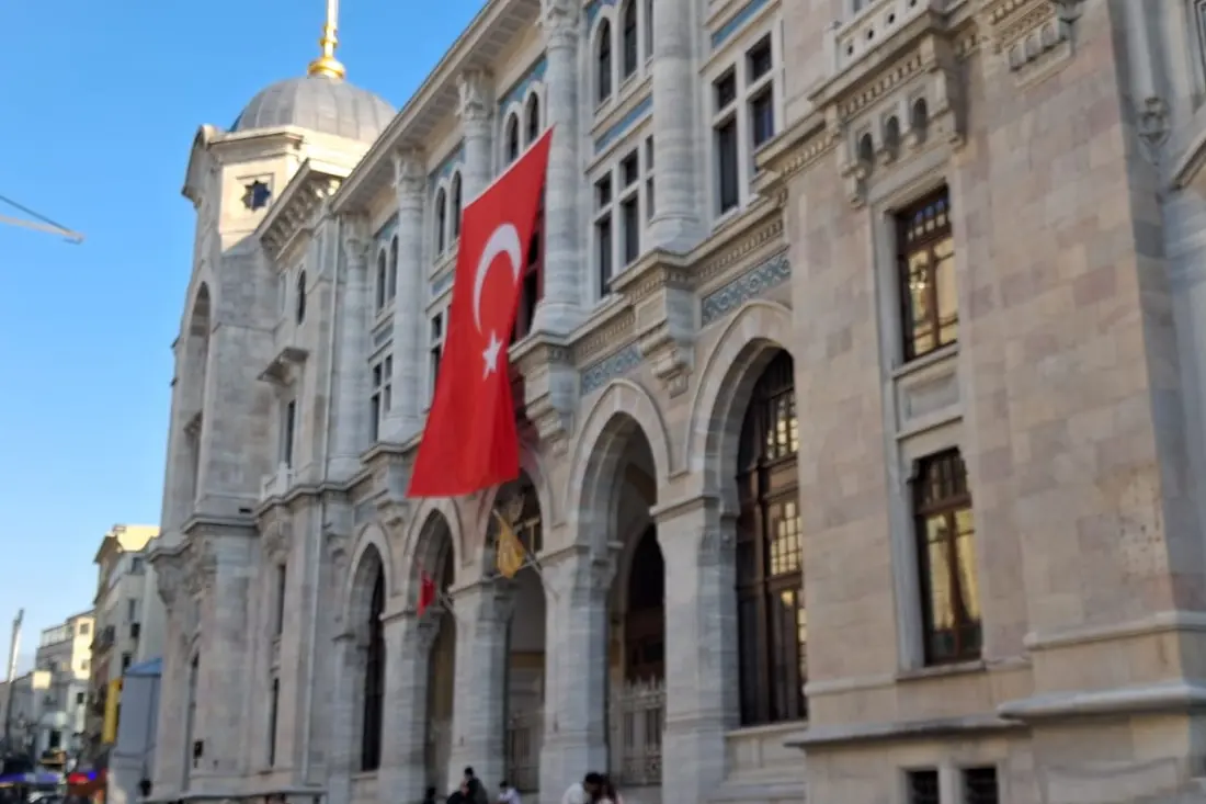 Kamienna fasada Głównego Urzędu Pocztowego Sirkeci z łukowymi oknami i turecką flagą.